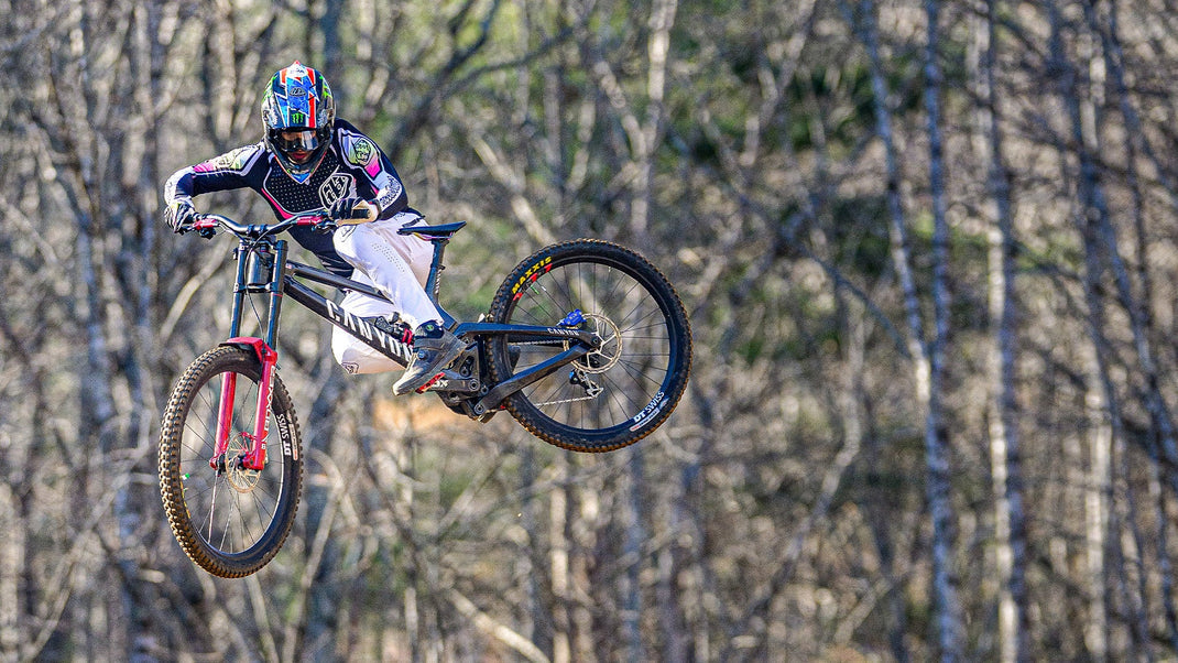 Troy Lee Designs mountain bike rider airborne on a forest trail